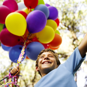 Young Boy Holding a String of Balloons --- Image by © Royalty-Free/Corbis